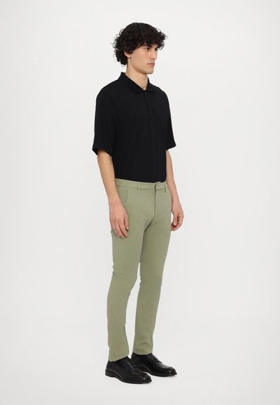 Svart kortärmad pikétröja, gröna slim fit-byxor, svarta skor. Enkla mönster med krage och naturliga texturer.