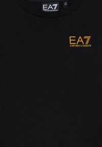 Svart t-skjorte med lite orange EA7 Emporio Armani-logo trykket på øvre venstre bryst under en svart krageetikett.