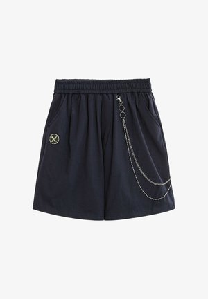 Pantalones cortos negros con cintura elástica, bolsillos laterales, cadena decorativa plateada en el lado derecho y un pequeño parche circular en el lado izquierdo.