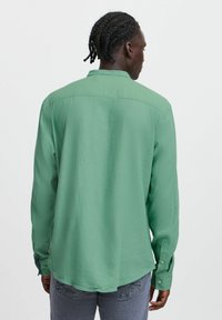Grøn langærmet skjorte med lige kant, knapmanchetter og en blød tekstur, båret over lysegrå jeans.