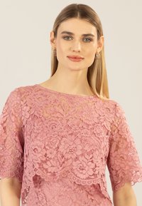 Rosa Spitze-Oberteil mit floralen Mustern, kurzen Ärmeln und Rundhalsausschnitt, mit transparentem Überzug und gewelltem Saumdetail.