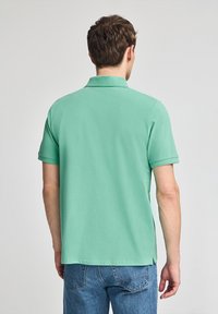 Camiseta polo verde menta hecha de una tela suave, con cuello y mangas cortas. La camiseta tiene un corte recto y un diseño sencillo.