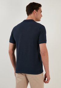 Polo de color azul marino hecho de algodón, con mangas cortas y un cuello clásico. Textura suave con un ajuste regular y un dobladillo recto.