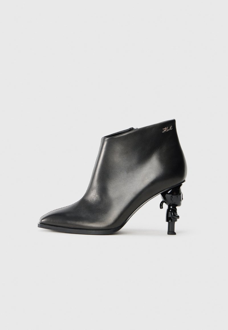 Black leather ankle boot with pointed toe, glossy finish, and distinctive sculptural heel featuring a figurine accent. Side zip closure.