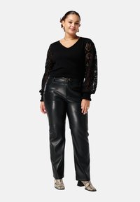 Zwarte gebreide trui met kanten details op de lange mouwen, gecombineerd met aansluitende zwarte leren broek en laarzen met slangenprint op hakken.