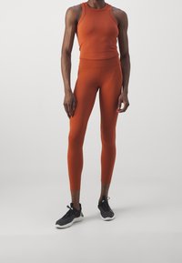 Orangefarbener Sport-Tanktop und Leggings aus elastischem Material, mit figurbetontem Schnitt. Schwarze Sportschuhe mit strukturierten Sohlen.