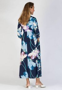 Kwiatowa maxi sukienka w kolorze granatowym z niebieskimi i fioletowymi wzorami kwiatów, z długimi rękawami i zwiewnym krojem; noszona z kremowymi butami na słupku.