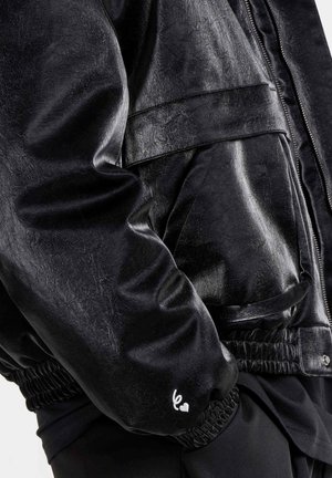 Zwarte bomberjas van imitatieleer met een gestructureerd oppervlak, elastische manchetten en een zijzak; heeft een klein wit geborduurd detail.