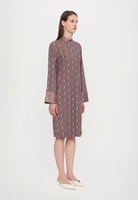 Langärmliges, knielanges Kleid in Mauve mit Diamantmustern in Schwarz und Hellgrün. Verfügt über einen hohen Kragen und eine lässige Passform.