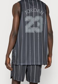 Conjunto de camiseta y pantalones cortos de baloncesto de malla negra con rayas blancas. Presenta "JORDAN" y "23" impresos en la parte posterior. Tela ligera y transpirable.