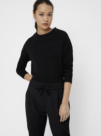 Suéter negro de punto con mangas largas y cuello redondo, combinado con pantalones gris oscuro con cintura ajustable y pliegues.