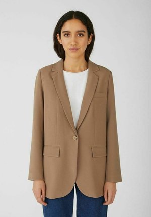Hnědý blazer vyrobený z hladkého materiálu s jedním knoflíkovým zapínáním, klopovými límci a dvěma předními kapsami. Nosený přes bílý top.