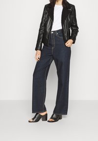 Zwarte leren jas met een nepbonten kraag, wit T-shirt, hooggepolsterde donkere denim wijde broek en zwarte open teens block-heeled muiltjes.