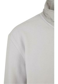 Lys grå fleecegenser med høy krage og en ujevn tekstur. Designet er minimalistisk uten tydelige mønstre eller detaljer.