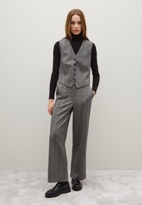 Completo in tessuto morbido con gilet a scacchi grigi e pantaloni a gamba larga. Il gilet presenta un collo a V e sei bottoni, abbinato a mocassini neri.