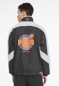 Juodas švarkas su baltais akcentais, turi oranžinį logotipą ant nugaros. Pagamintas iš lengvos medžiagos, turi apykaklę ir elastingas rankoves.