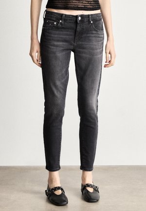 Jeans skinny noirs avec une texture décolorée, design à cinq poches et passants de ceinture. Associés à des chaussures plates noires avec des straps décoratifs.