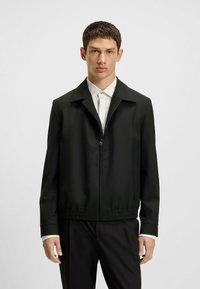 Black zip-up jacket with a collared design, elastic waistband, and smooth, lightweight fabric. Features side pockets and tailored fit.