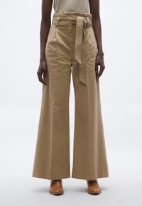 Pantaloni kaki cu picioare largi și talie cu curea, realizați dintr-un material neted. Au buzunare laterale și tiv curat. Purtați cu pantofi maro cu toc.