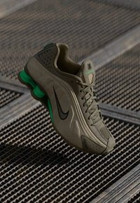 Baskets Nike avec un dessus vert olive clair et des perforations, un swoosh noir, des accents verts au talon et un design de semelle texturé.
