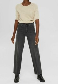 Haut en maille à manches courtes de couleur beige associé à un jean taille haute, coupe large, gris foncé, et des bottines noires. Tissu lisse avec texture classique du denim.