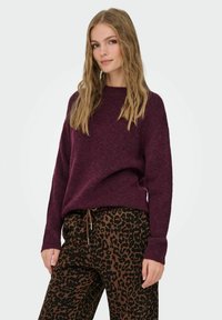 Burgunderfarbener Strickpullover mit lockerer Passform und Rundhalsausschnitt, kombiniert mit braunen Leopard-Print-Hosen mit einem Kordelzugbund.