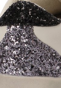 Zapatilla blanca con un diseño texturizado que presenta acentos brillantes en negro y plata. Parte superior de cuero suave con un detalle de apliqué brillante en contraste.