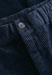 Marine corduroy stof met verticale ribbels; bevat een zilveren knop met vier gaten. Close-up met details van textuur en stiksels.