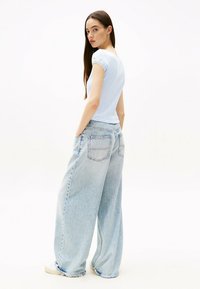 Top azzurro chiaro a costine con maniche corte arricciate abbinato a jeans oversize in lavaggio chiaro con tasche posteriori e vestibilità rilassata.