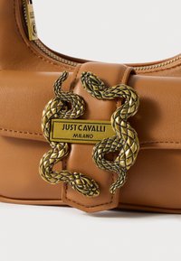 Braune Kunstleder-Handtasche mit einem zentralen Verschluss, der verschlungene Schlangen zeigt, goldfarbenen Beschlägen und einem rechteckigen Markenschild.