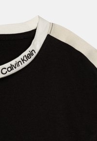 Črna bombažna majica s kontrastnim belim okroglim izrezom. Na ovratniku se nahaja "Calvin Klein" logo v črni niti. Gladka tekstura.