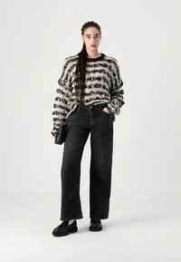 Black and white striped knitted sweater with a loose fit, paired with high-waisted black denim jeans and chunky black shoes.
