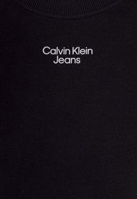 Tela negra con el texto blanco "Calvin Klein Jeans" centrado cerca del cuello en una prenda de cuello redondo.