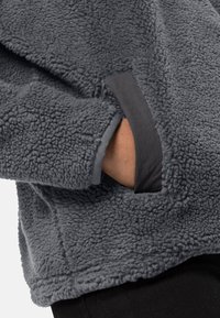 Pullover in pile grigio con superficie testurizzata, dotato di una finitura a contrasto grigio scuro lungo i polsini e di una tasca laterale.