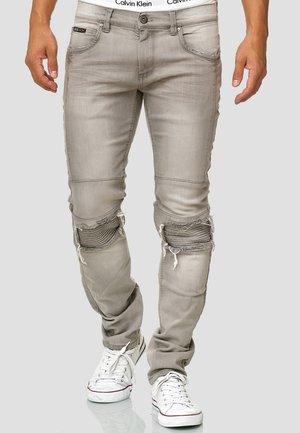 Graue Slim-Fit-Jeans mit abgenutzten, gerippten Knie-Patches, getragen mit weißen Turnschuhen und sichtbarem Calvin Klein Bund.