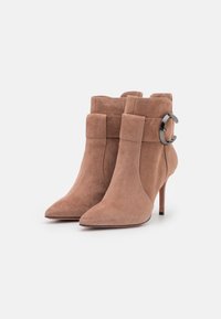 Bottines en velours de couleur brun clair, avec un bout pointu, un talon effilé et des accents métalliques sur le côté pour plus de détails.
