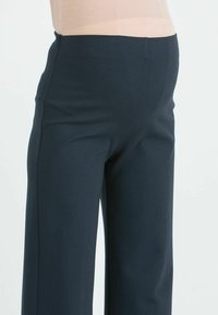 Tummansiniset housut, joissa on sileä pinta, korkeavyötäröinen malli ja tyylikäs istuvuus, suunniteltu puhtaaksi ja moderniksi siluetiksi.