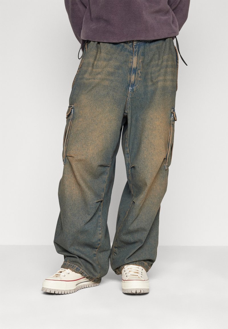 Volné cargo džíny v bledě modrém denimu, s kapsami na zip a pasem na šňůrku. Kombinované s bílými teniskami.