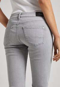 Jeans de mezclilla gris con un diseño ajustado, que presentan bolsillos traseros estándar y sutiles acentos de costura. La tela tiene una textura suave.