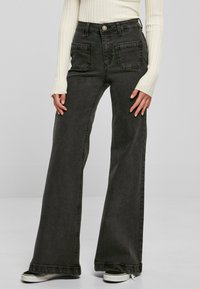 Jeans negros acampanados con bolsillos frontales, cintura alta y un ligero desvanecimiento. Terminados con un dobladillo limpio y combinados con una blusa de manga larga de canalé color crema.