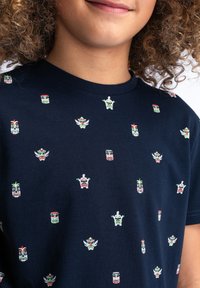 Camiseta de algodón azul marino con un patrón repetido de coloridas máscaras estilizadas en verde, rojo y blanco, con un diseño de cuello redondo.