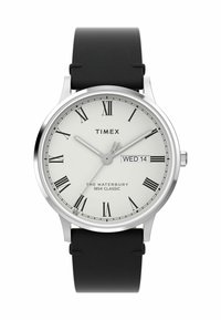 Timex Waterbury watch features a round silver stainless steel case, white dial with Roman numerals, black leather strap, and date display.
