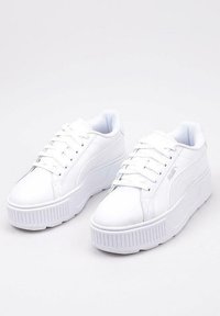 Białe sneakersy z gładką syntetyczną cholewką, sznurowanym zapięciem oraz masywną gumową podeszwą z teksturowanym wykończeniem.