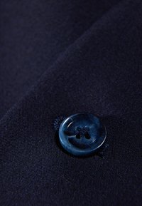 Marineblaue Stoff mit einer glatten Textur und einem auffälligen runden blauen Knopf, der zwei Löcher und eine subtile Nahtdetail aufweist.