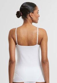 White tank top with thin adjustable straps, made of a soft, smooth cotton blend. Features a fitted design ending at the hips.