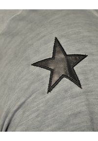 Grått tyg med en strukturerad yta som har en svart broderad stjärndesign. Stjärnan har en lätt glans och är inramad med svart söm.