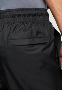 Svarta träningsshorts med elastisk midja, som har en sidoficka, slät textur och minimalistisk design.