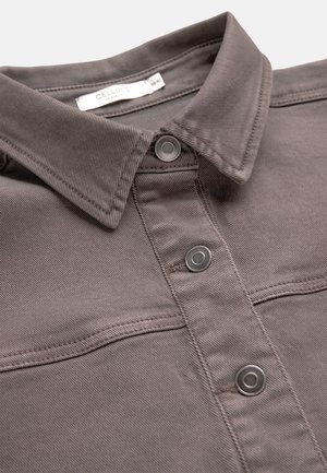 Grauer Baumwollhemdkragen mit drei sichtbaren Metall-Druckknöpfen und einem eingenähten weißen Pflegeetikett im Halsausschnitt.