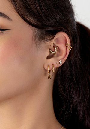 Ear with six gold and diamond earrings, including a star charm, twisted hoop, floral hoop, and small gem studs on dark-haired person.