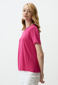 Korte mouwen, ronde hals t-shirt in felle roze stof, gladde textuur, ontspannen pasvorm, gecombineerd met witte broek, met een eenvoudig ontwerp.